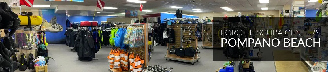 Panoramic interior of the Force-E dive shop, with racks of wetsuits, fins, masks and regulators, dive flags, and a sea turtle mural, overlaid with the words Force-E Scuba Centers Pompano Beach