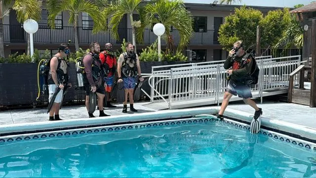 An instructor in full scuba gear steps off the pool edge to demonstrate the giant stride entry