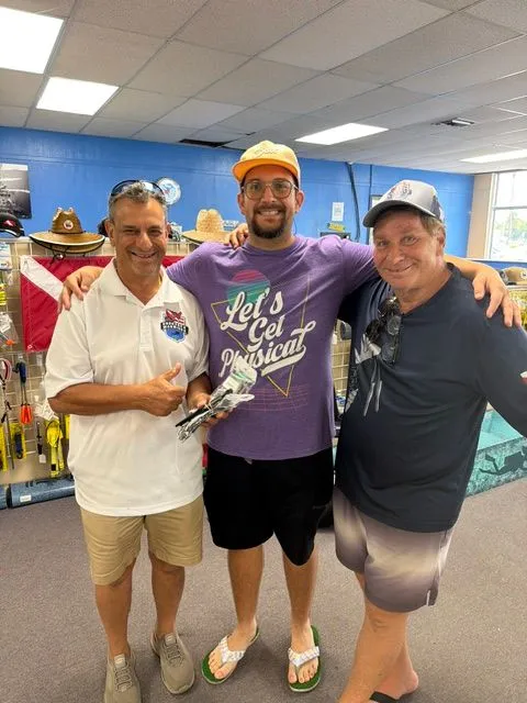 Three men smiling together inside a dive shop after a scuba certification