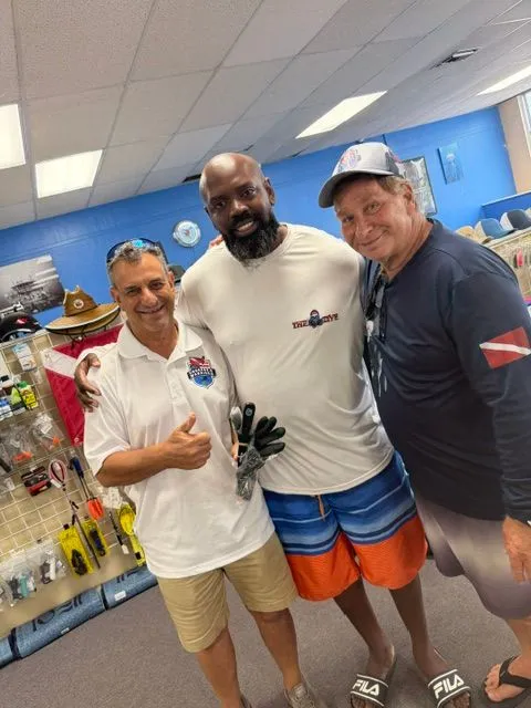 Three men smiling together inside a dive shop after a scuba certification