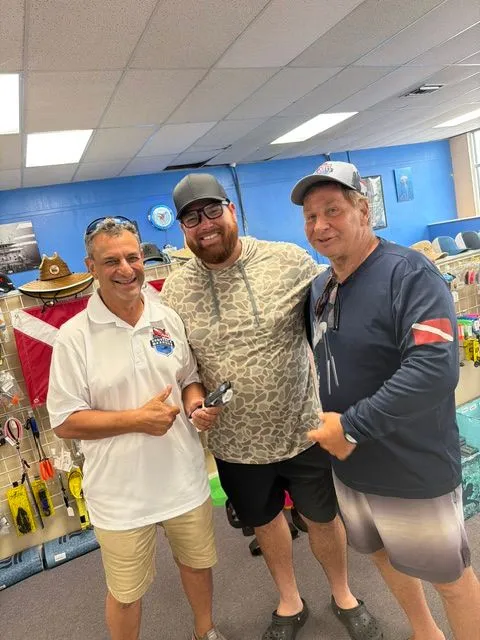 Three men smiling together inside a dive shop after a scuba certification